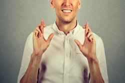 Cropped photo of smiling white man in a cream polo shirt with fingers crossed on both hands as if for good luck